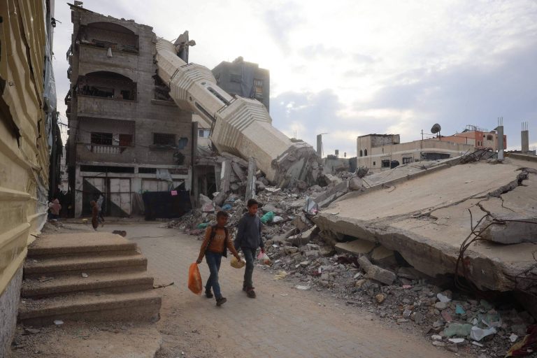 Crianças palestinas carregam comida em meio a edifícios destruídos na Faixa de Gaza