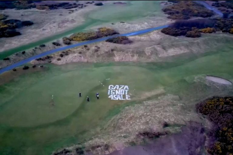 A imagem mostra um campo de golfe com uma mensagem escrita em letras grandes no gramado que diz