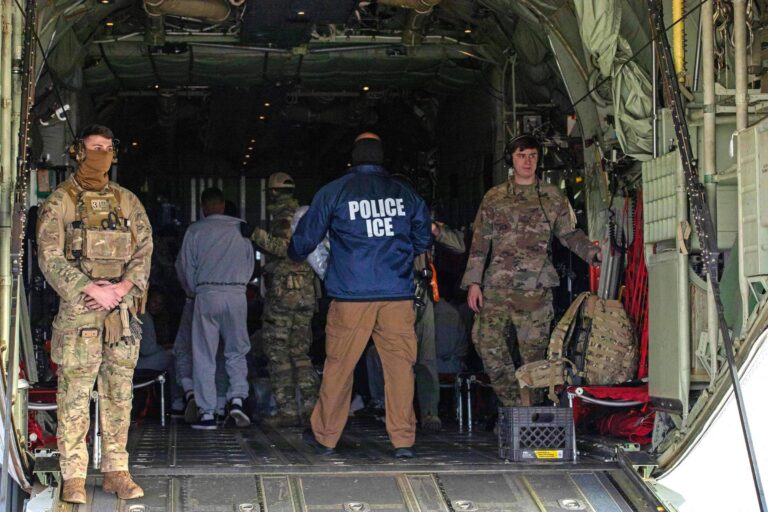 Em primeiro plano, veem-se dois soldados americanos, de uniforme militar. Ao fundo, um homem aparece de costas, com um colete escrito