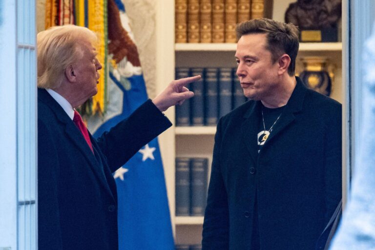 A imagem mostra duas pessoas em um ambiente que parece ser o Salão Oval da Casa Branca. Uma das pessoas está vestida com um terno escuro e uma gravata vermelha, enquanto a outra usa um casaco preto e um colar. A pessoa de terno está apontando para a outra, que parece estar ouvindo atentamente. Ao fundo, há estantes com livros e uma bandeira dos Estados Unidos.
